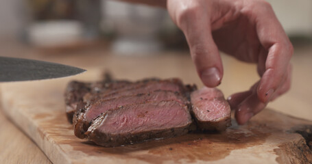 man moving piece of medium rib eye steak meat on side on board, wide photo