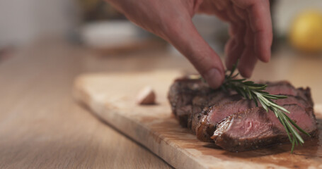 man decorating sliced medium rib eye steak with rosemary branch, wide photo