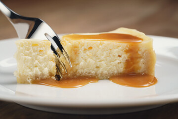 cheesecake with caramel sauce on plate closeup eaten with fork, shallow focus