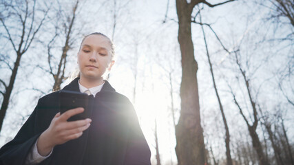 low angle shot of female teen girl using smartphone standing on town alley in spring sunny day, wide photo