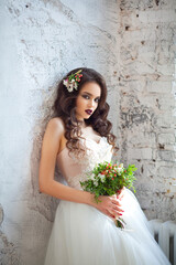 Portrait of a beautiful young girl of European appearance in a stylish white wedding dress with a hairdo and makeup with a wedding bouquet in the hands of fine flowers