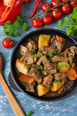 Meat goulash with vegetables, potatoes and mushrooms on concrete, grunge background