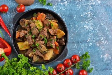 Meat goulash with vegetables, potatoes and mushrooms on concrete, grunge background