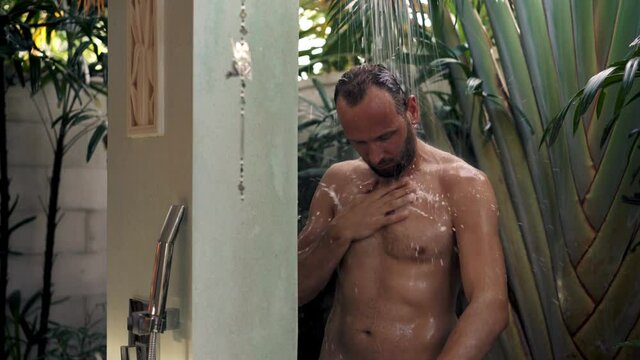Young man washing body under shower in open bathroom, 4K
