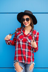 Portrait of beauty fashion smiling hipster girl in hat and sunglasses on blue background