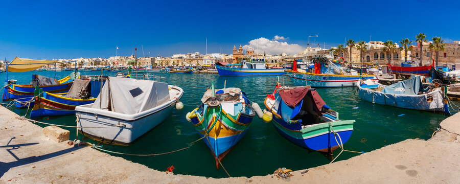 Panorama with traditional eyed colorful boats Luzzu in the Harbor of Mediterranean fishing village Marsaxlokk, Malta