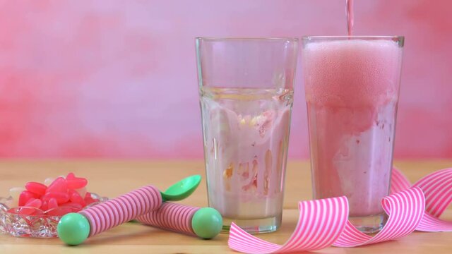 4k Making ice cream soda floats with pink raspberry soda and ice cream in tall cafe glasses against a pink theme summer party backgroud, filling glasses with soda.