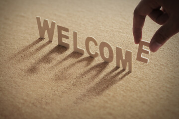 WELCOME wood word on compressed board with human's finger at E letter