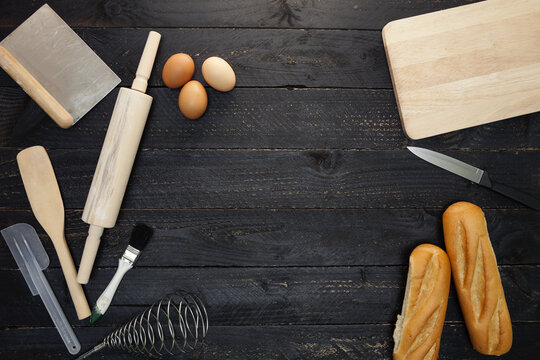 Baking background with bread, rolling pin,eggs,wooden spoons on black wooden background,cooking concept top view.