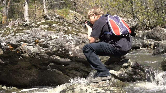 Young Blond Photographes Forest Stream. Early Spring is a Sunny Day, a Large Stream of Water.