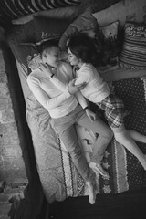 Naklejka na ściany i meble Young couple staying at home together on holiday evening and lying on bed with christmas bed linen. Young lovers ib cute pullovers hugging and relaxing. Top view