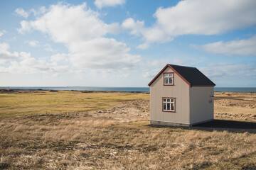 A small house to the right on a grassy coastal edge with a big blue sky layered with soft clouds
