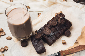 Chocolate brownie on wooden chopping board. Plain cake on rustic table. Grey napkin and baking paper, knife and glass of cocoa milk. Selective focus