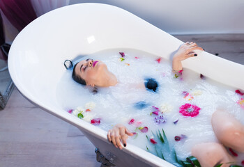 Woman in bath. Sexy brunette woman relaxing in hot milk bathtube with flowers. she is wearing black sexual lingerie. Spa satisfaction