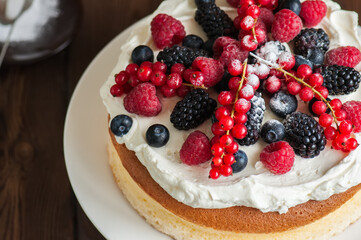 Close up of fluffy Japanese cotton cheesecake with wipped cream cheese frosting and garnished with forest berries served on a plate over wooden background. Rustic style