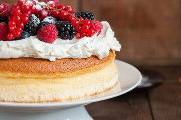 Close up of fluffy Japanese cotton cheesecake with wipped cream cheese frosting and garnished with forest berries served on a plate over wooden background. Rustic style
