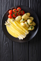 asparagus served with hollandaise sauce, new potatoes and tomatoes close-up. vertical top view