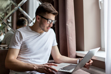 Handsome bearded man sitting on the couch and working with a laptop. man wearing glasses.