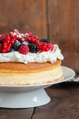 Close up of fluffy Japanese cotton cheesecake with wipped cream cheese frosting and garnished with forest berries served on a plate over wooden background. Rustic style