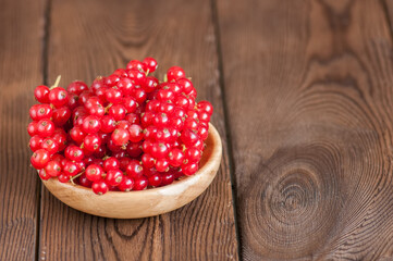 Close up of heap of fresh raw red currants in a plate on a wooden background. Copy space.