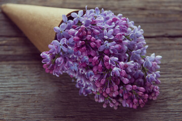 Lilac flowers bouquet in a craft paper cornet on the old wooden background