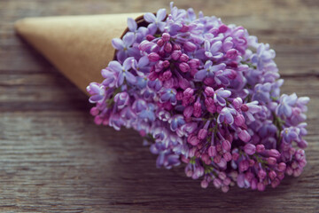 Lilac flowers bouquet in a craft paper cornet on the old wooden background