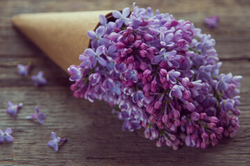Lilac flowers bouquet in a craft paper cornet on the old wooden background