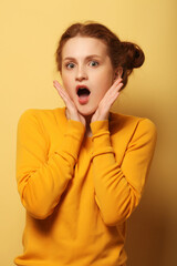 Beautiful young surprised redhair woman over yellow background