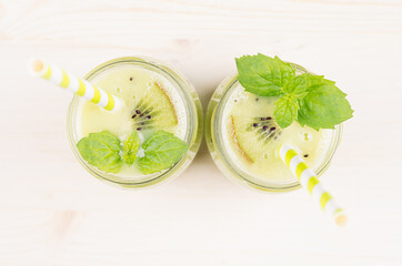 Freshly blended green kiwi fruit smoothie in glass jars with straw, mint leaf, top view. White...