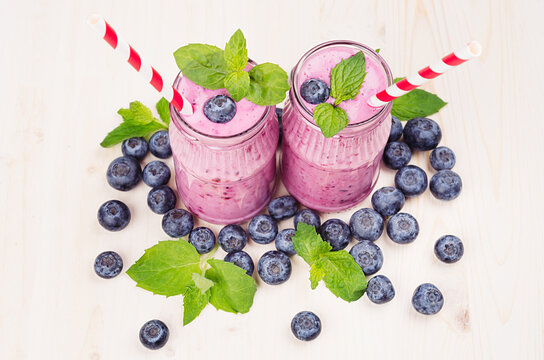 Violet blueberry fruit smoothie in glass jars with straw, mint leaves, berries, close up. White wooden board background.