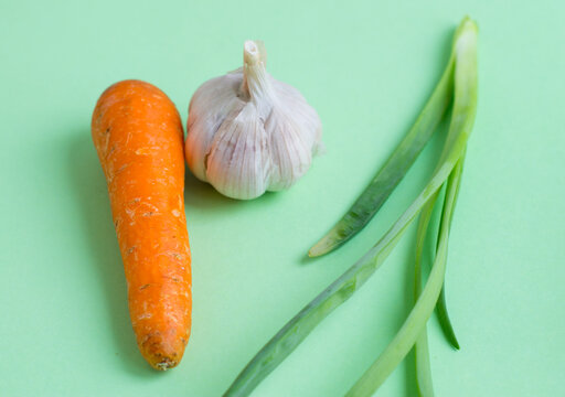 Fresh vegetables on a light green background. Carrot, onion, garlic