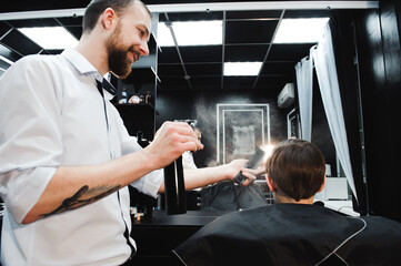 Young handsome barber making haircut of cute boy in barbershop