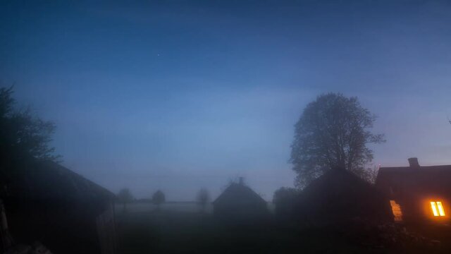 Night timelapse of misty fog blowing over building  at dusk. Night sky with stars.