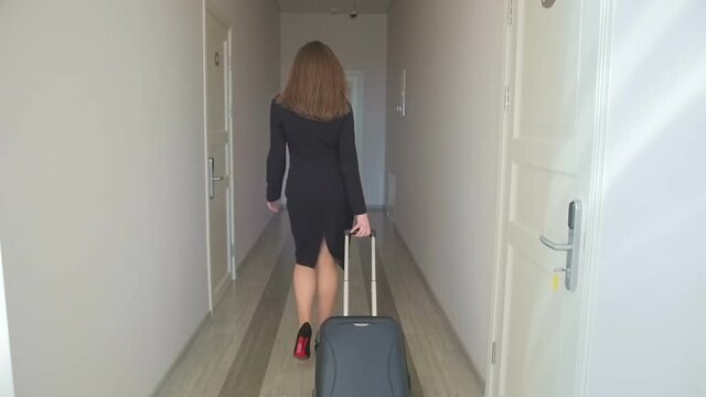 Slow motion footage of elegant businesswoman walking with suitcase at hallway