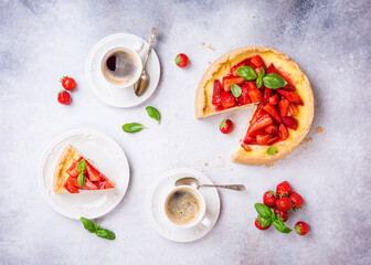 Overhead shot of cups of coffee, delicious homemade strawberry cheesecake and flowers on light gray background. Top view, flat lay.