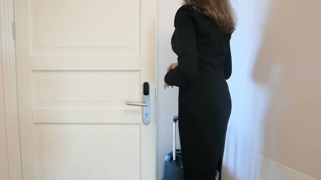 Slow motion video of young woman with suitcase opening door and entering hotel room