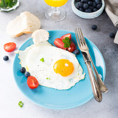 Fried egg on blue plate, tomatoes, blueberries, mint tea and orange juice. Healthy breakfast concept.