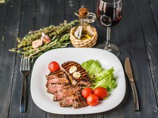 Delicious Beef steak with rosemary and thyme, lettuce, cherry tomatoes and red wine.