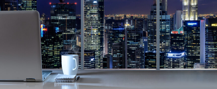 Laptop on table in office with panoramic night view of modern downtown skyscrapers at business district