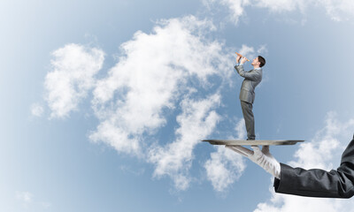 Businessman on metal tray playing fife against blue sky background