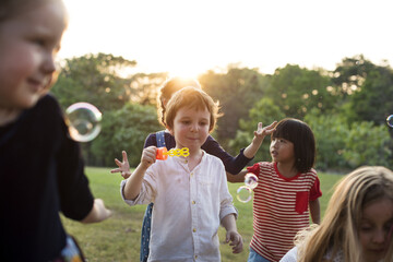 Fototapeta premium Group of kindergarten kids friends playing blowing bubbles fun