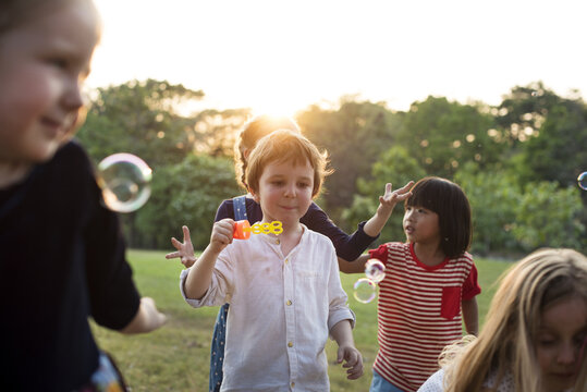 Group of kindergarten kids friends playing blowing bubbles fun