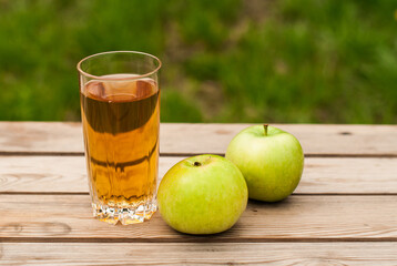 Fresh apple juice and green apples on a wooden table in the garden.