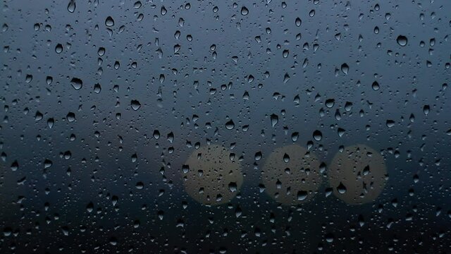 Drops of rain flow down the window glass at afterdark