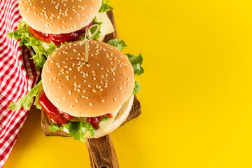 Tasty fresh unhealthy hamburgers with ketchup and vegetables on yellow vibrant bright background. Top View with Copy Space.