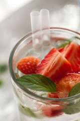 Tasty fresh cold drink with ice, water, mint and strawberry in glass. Closeup.