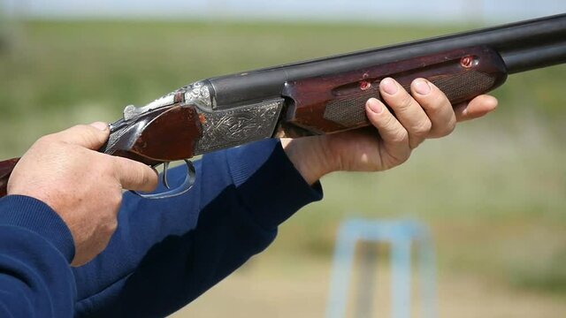 Sportsman stands in profile and shoots from a decorated double barrel shotgun, while practicing skeet shooting and aiming at clay targets in a sunny day in autumn in slow motion