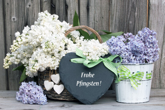 Text "Frohe Pfingsten" auf Schieferherz mit Flieder rustikal vor Holzhintergrund
