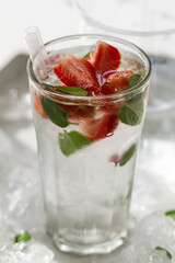 Tasty fresh cold drink with ice, water, mint and strawberry in glass. Closeup.