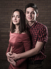 Cheerful young couple in love stand and smile in a red brick studio